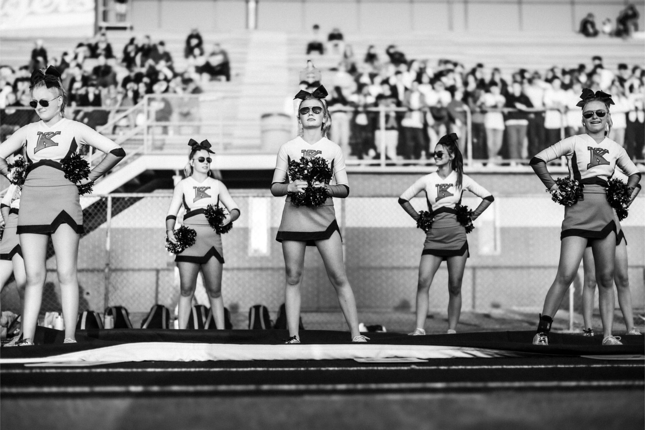  Five high school cheerleaders in uniform stand on the sideline of a football game, the kind of school sports community that often runs a sales fundraiser.