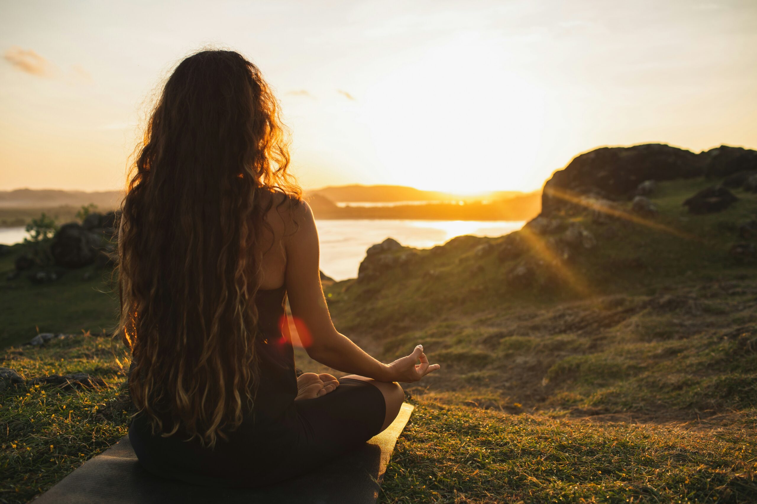 Woman practicing sunrise yoga on a hilltop overlooking water, symbolizing a peaceful start to a solstice fundraiser