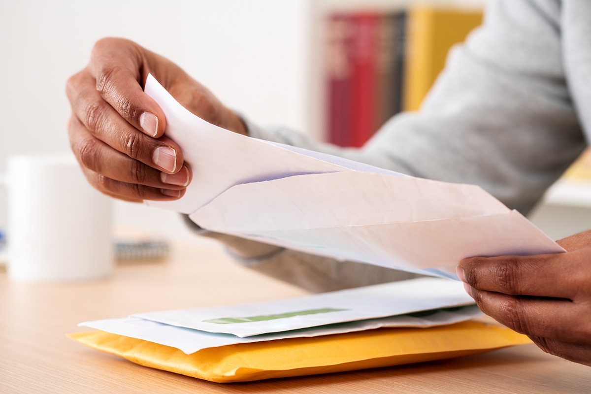 Person opening direct mail envelope at desk with stack of colorful letters and postcards