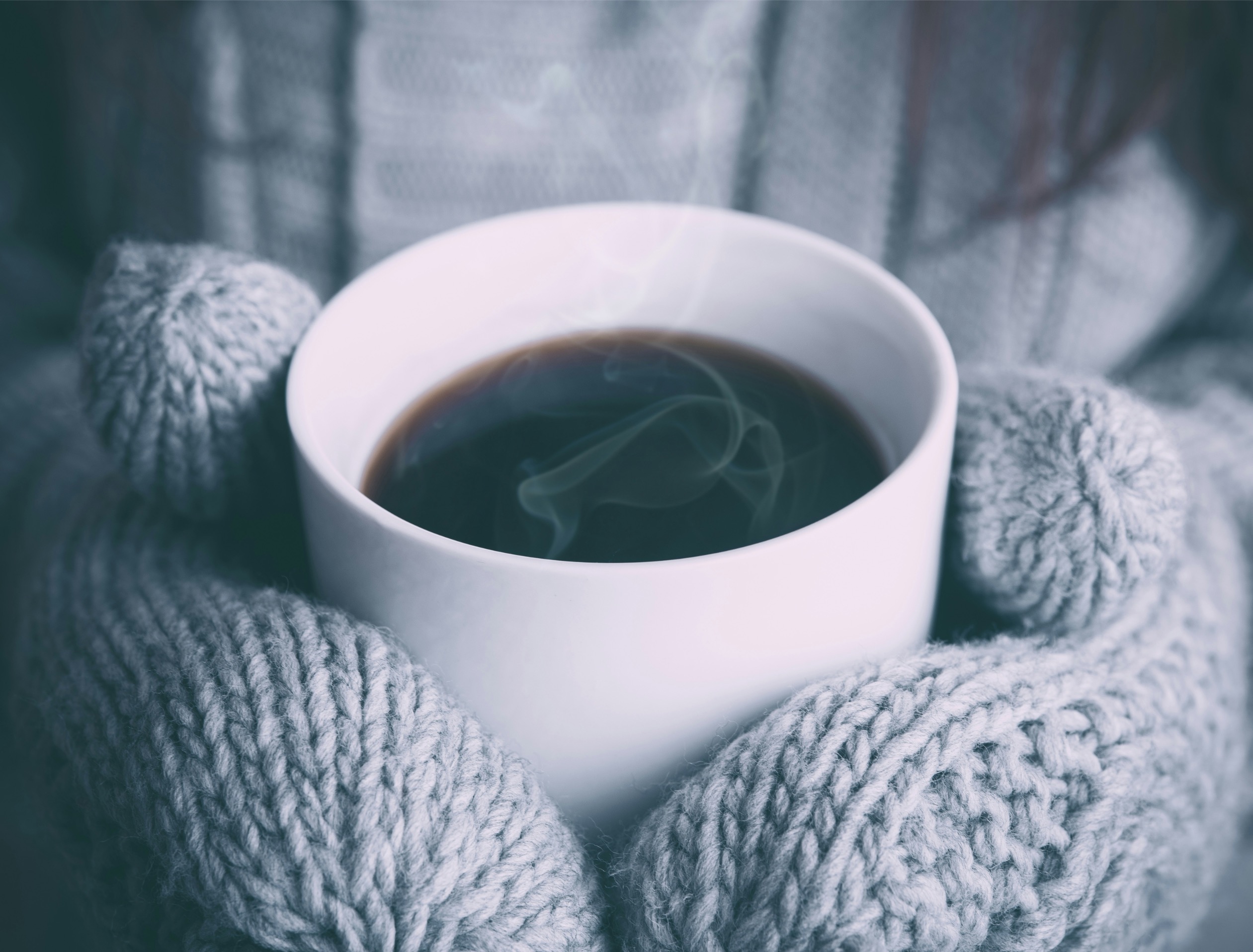 cozy-winter-fundraising-hero Hands in knitted mittens holding a steaming mug of coffee or hot chocolate on a cold winter day